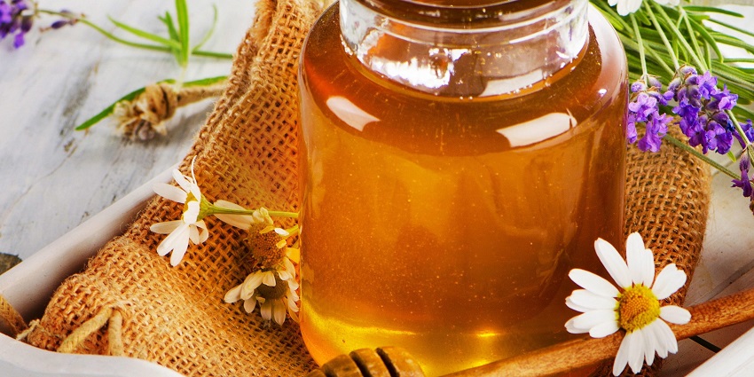 picture of honey on a table beside flowers 