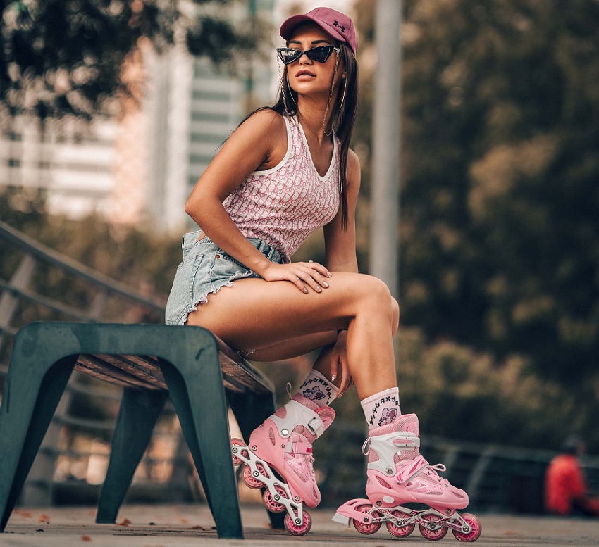 picture of a woman in pink top, shorts and pink roller blades sitting on a bench in the park 