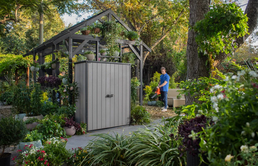 slim garden storage shed with man blowing leaves in the background 