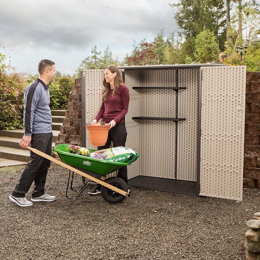 couple placing things in wheelbarrow in front of a slim garden storage shed 